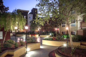 Exterior of building at night with lighted path, greenery, and trees