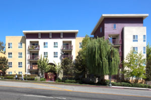 Exterior shot from street with balconies, trees, and people walking on sidewalk