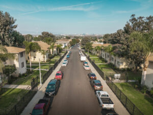 car lined street, exterior of building surrounded by grass and palm trees on sunny day, aerial view