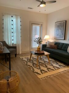 living room, wood-like floors, couch, end table, balcony door, window.