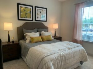 bedroom, queen-sized bed neutral toned carpeting, window right side of bed.