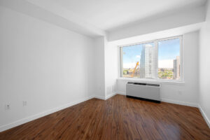 Unit Bedroom, hardwood floors, AC/furnace in front of window, nearly wall to wall windows.