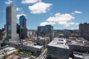 Unit view of city from terrace, sprawling skyline, residential and industrial buildings in view. Photo taken on a partly cloudy sunny day.