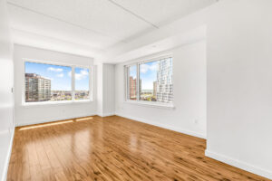 Unit Living room, large windows on both far side walls, hardwood floors, white walls.