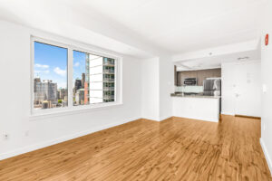 Unit Living room with view of kitchen and entry door, large window where couch or dining table could go.