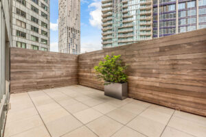 Unit patio, wooden fence, view of buildings above fence, concrete floor, large metal box planter.