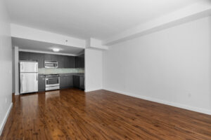 Unit Living room, Hardwood floors, white walls, open floorplan kitchen/living room.