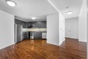 Unit Kitchen/Living room, stainless steel appliances, storage closet adjacent to kitchen and living room, hardwood floors, ceiling light fixtures, open concept floorplan.