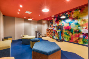 Community Kids Room, multicolored walls, salmon colored ceiling, children’s playset, children’s Basketball hoop, Hexagonal furniture, misc. toys.