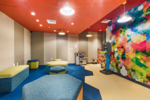 Community Kids Room, multicolored walls, salmon colored ceiling, children’s playset, children’s Basketball hoop, Hexagonal furniture, misc. toys.