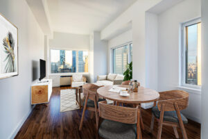 Unit Living room, right to left; 4 seat dining table, couch and 2 lounge chairs behind dining table, tv parallel to couch (left wall tv, right wall couch), windows along each wall except left wall in photo, hardwood floors, are rug beneath couch and chairs.