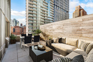 Unit terrace, Furnished, outdoor sectional with end-table and matching outdoor coffee table, outdoor dining table and furniture opposite end of sectional, potted plants on both sides of dining table, wooden fencing for privacy.
