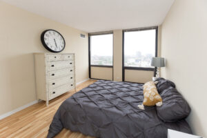 Unit Bedroom, Furnished, queen size bed, 2 nightstands, wood floors, large dresser, 2 large windows with view of downtown.