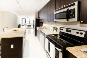 Unit Kitchen, stainless steel appliances, wood floors, kitchen island, open floor plan, granite countertops, dark brown cabinetry.