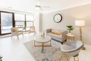 Unit living room, wood floors, large colorful area rug, contemporary furniture, fan in living room, tan colored walls.