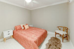 Unit bedroom, wood floors, chair in corner, queen size bed, 2 nightstands on both sides of the bed.