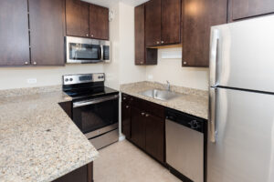 Interior Kitchen, granite countertops, stainless steel appliances, tile floor. dark brown cabinetry.