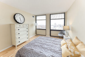 Unit Bedroom, queen sized bed, 2 nightstands, chair in corner of room by windows, 2 large windows with view of downtown chicago.