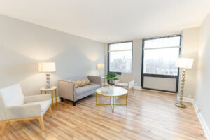 Unit Living room, 2 person couch and 2 chairs surrounding large coffee table, wood floors, 2 large windows, 2 end tables on both sides of couch.