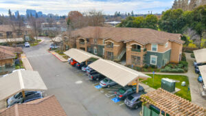 Aerial Exterior, parking lot, covered parking, green and beige residential buildings, skyline in background, photo taken in winter.
