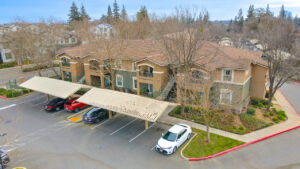 Aerial Exterior, parking lot, covered parking, meticulous landscaping ,green and beige residential buildings, photo taken in winter.
