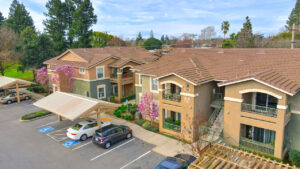 Aerial Exterior, parking lot, covered parking, meticulous landscaping ,green and beige residential buildings, photo taken in winter.