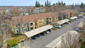 Aerial Exterior, parking lot, covered parking, meticulous landscaping ,green and beige residential buildings, photo taken in winter.