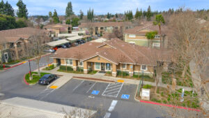 Aerial Exterior of leasing office, meticulous landscaping, parking in front of office, photo taken in winter.