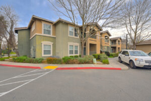 Exterior green and beige residential building, parking out front, meticulous landscaping, photo taken on a sunny day.