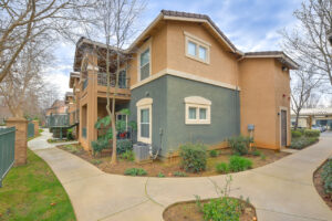 Exterior Green and beige residential building, two story walk up, meticulous landscaping, balconies on all units, photo taken on a sunny day.