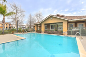 Exterior Swimming pool, leasing office attached, fence around swimming pool, meticulous landscaping surrounding the fence, photo taken on a sunny day.