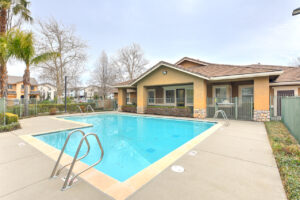 Exterior Swimming pool, leasing office attached, fence around swimming pool, meticulous landscaping surrounding the fence, photo taken on a sunny day.