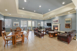 Interior Rivers Senior community room, fireplace, leather couches, coffee table with puzzle on it, rustic decor, two four seat tables.