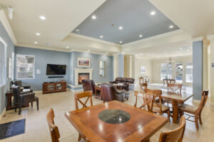 Interior Rivers Senior community room, fireplace, leather couches, coffee table with puzzle on it, rustic decor, two four seat tables.
